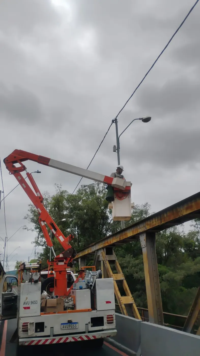 Profissional no cesto aéreo fazendo manutenção de iluminação pública sobre uma ponte